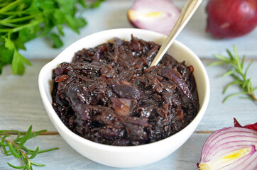 Jam of red onion in a white bowl on a light wooden background