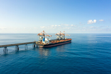 Obraz premium Coal carrier Cargo Ship docked at a commercial pier during unloading operation, Aerial view. 