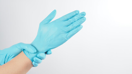 Left hand is pulling blue latex gloves on white background.
