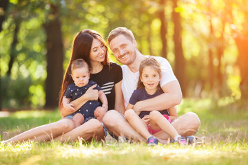 Happy mother, father, son and daughter in the park. Beauty nature scene with family outdoor lifestyle. Happy family resting together sitting on the grass, having fun outdoor. Happiness and harmony