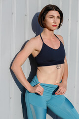 Tough young woman in sports wear staring at camera. Sportswoman taking a breather after training outdoors.