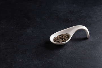 Black caviar in white spoon on black background. Ceramic spoon with sturgeon caviar. Copy space.