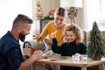 Family with small daughter indoors at home at Christmas, making Christmas cards.