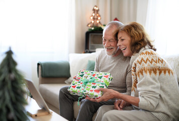 Side view of senior couple indoors at home at Christmas, having video call with family.