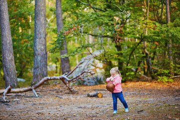 Naklejka na ściany i meble Adorable toddler girl with basket picking mushrooms in autumn forest