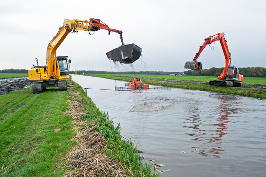 Dreding of an inland canal by two cranes; a silt pusher boat pushes the sediment towards the crane; sediment is dispursed on land. 