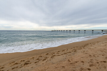 View of footsteps on the beach, with a walkway in the background, a cloudy day, in Badalona, Spain, horizontal