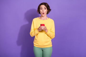 Photo of astonished girl hold smartphone wear yellow sweater green trousers isolated over purple...