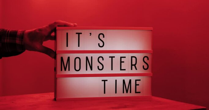 It's Monsters Time text displayed on a LED light box on the table man turning the light on, red light in the room, medium close-up, eye level 4k cinematic 