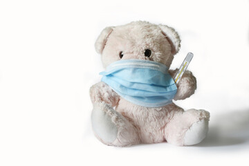 Soft toy pink bear measuring temperature with a medical thermometer in a medical mask on a white background