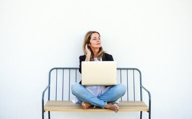 Fototapeta na wymiar Mature woman working in home office outdoors on bench, using laptop.