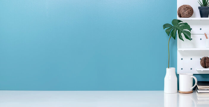 Mockup creative workspace with white ceremic vase, white mug and houseplant on white top table and blue wall background.