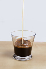 Vertical shot of pouring milk into an espresso coffee