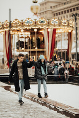Happy couple are walking near the carousel. A traveling couple walking on a snowy cold winter day.