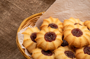 Homemade pastry cookies with jam in a wicker basket on a background of homespun fabric with a rough texture, close-up, selective focus.