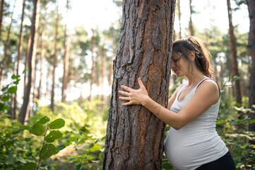 Portrait of meditating pregnant woman outdoors in nature, hugging tree.