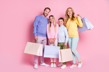 Full size photo of positive family daddy mommy small kids boy girl hold shopping bags isolated over pastel color background