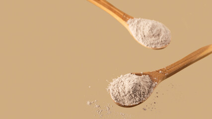 Dry clay for face mask in wooden spoons on neutral beige background. Self care concept. Copy space