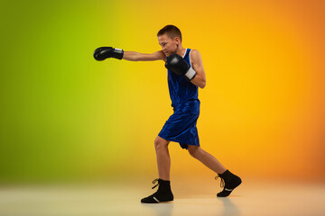 On the go. Teenage professional boxer training in action, motion isolated on gradient background in neon light. Kicking, boxing. Concept of sport, movement, energy and dynamic, healthy lifestyle.