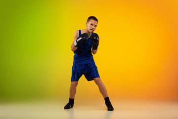 Emotional. Teenage professional boxer training in action, motion isolated on gradient background in neon light. Kicking, boxing. Concept of sport, movement, energy and dynamic, healthy lifestyle.