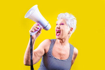 Senior woman screaming loudly in a megaphone on yellow background -Elderly beautiful grey-haired woman demonstrating using megaphone over isolated yellow background