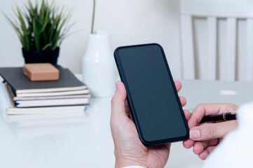 Cropped image of man hands holding blank screen smartphone while sitting at the table in office.