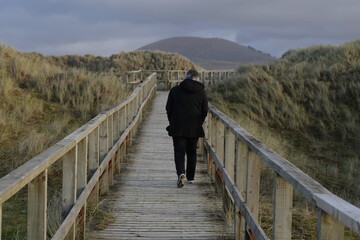 Fototapeta na wymiar A person walking along the wooden boardwalk between the sand dunes at Dyffryn Ardudwy, Gwynedd, Wales, UK.
