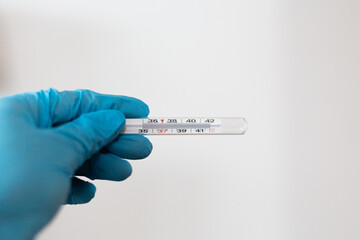 Obraz premium Close-up of medical thermometer being held by hand with protective blue rubber glove. Isolated against white background. 