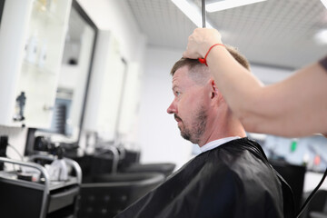 Fototapeta na wymiar Young man sits in hairdressing chair and makes haircut in beauty salon portrait. Small business development hairdressing services concept.