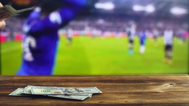 A man counts money dollars on the background of a football game on TV. Concept of bookmakers and sports betting, copy space for text