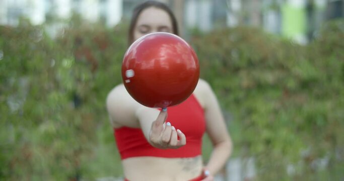 Woman in red sports costume holds callisthenic spinning ball on her finger, sports in the urban environment outdoors, gymnastics in the city, 4k 120p Prores HQ