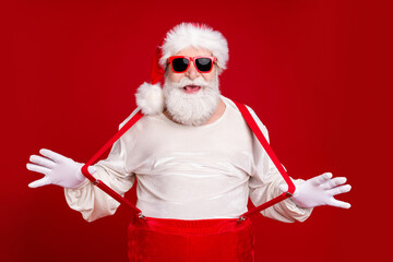 Fototapeta na wymiar Portrait of his he nice handsome cheerful cheery glad childish bearded Santa pulling suspenders having fun good mood newyear look outfit isolated bright vivid shine vibrant red color background