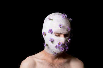 a portrait of a guy his head is wrapped in a bandage, flowers stick out of the bandage