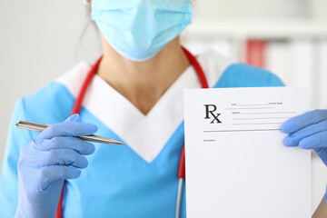 Doctor in protective mask on his face holds ballpoint pen and recipe closeup. Prescription drugs concept.