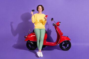 Fototapeta na wymiar Full length body size view attractive cheerful glad girl sitting on bike using gadget bank plastic card order app shop isolated over bright vivid shine vibrant lilac violet purple color background