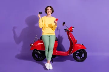 Foto op Plexiglas Full length body size view attractive cheerful glad girl sitting on bike using gadget bank plastic card order app shop isolated over bright vivid shine vibrant lilac violet purple color background © deagreez