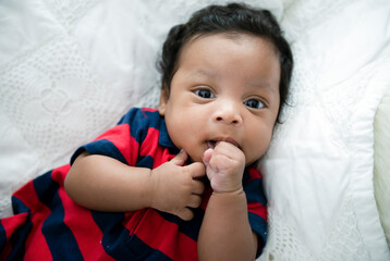 Portrait of little cute mixed-race baby 2 months old lying on white blanket looking and smiling at...