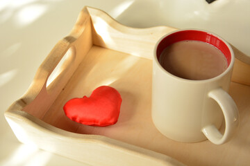 Cup of coffee and a small red heart on a wooden tray on a light background close up