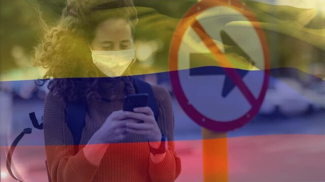 Colombian flag waving against woman wearing face mask using smartphone