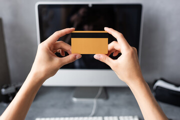 Cropped view of teleworker holding credit card near computer at home