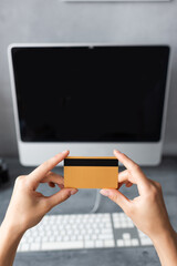 Cropped view of woman holding credit card near computer at home