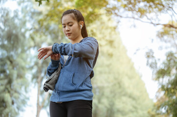 The asian woman looked down at the clock and pressed the clock stop after running to the natural park.
