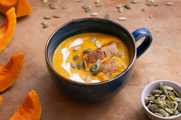 Pumpkin and carrot soup with cream on wooden background.  
Soup serving.