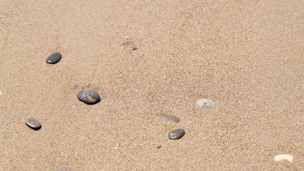 Fototapeta na wymiar Small gray wet stones on golden beach sand. Copy space. Wet sand and small stones on the seashore