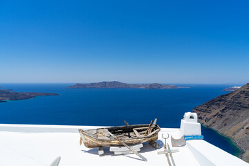 Old boat for decoration on a white roof of a house of Santorini island, Greece. Blue Mediterranean sea and Santorini caldera in the background