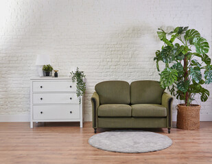 Green sofa and white cabinet in the room, vase of plant brick wall and frame.