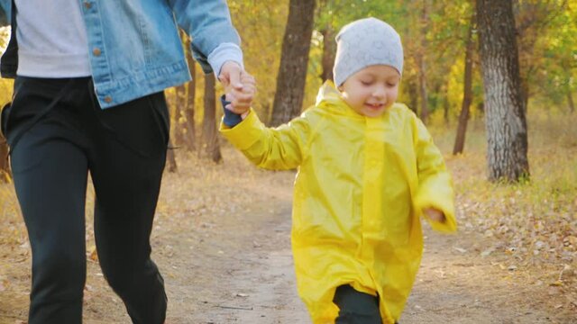 Young mother walking with a little son in autumn park. Happy family in autumn park. Happy family in nature concept. 4K slow motion.