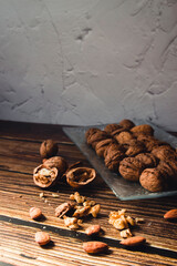 Glass plate full of walnuts on a wooden table. Walnuts receive the sun's rays. Vertical photography, concept of autumn and healthy food. Copy space