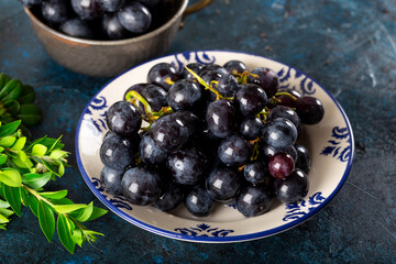Fresh black grapes and leaves in dish on dark background.