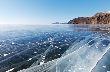 View of the vast expanses of frozen Baikal Lake on a sunny cold February day. Beautiful winter landscape with transparent smooth ice near the rocky coast. Travel on ice. Natural winter background